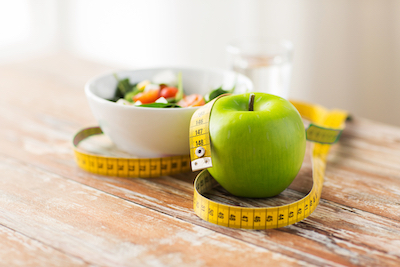 Bowl of salad and an apple with a tape measure 